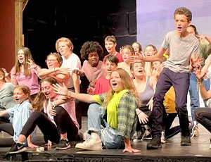 A group of campers perform together on stage during a theater production