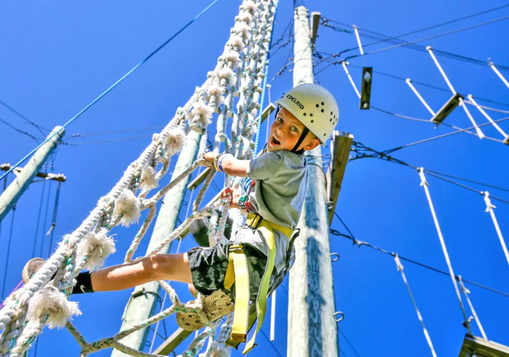 Boy pushing himself on ropes course at summer camp