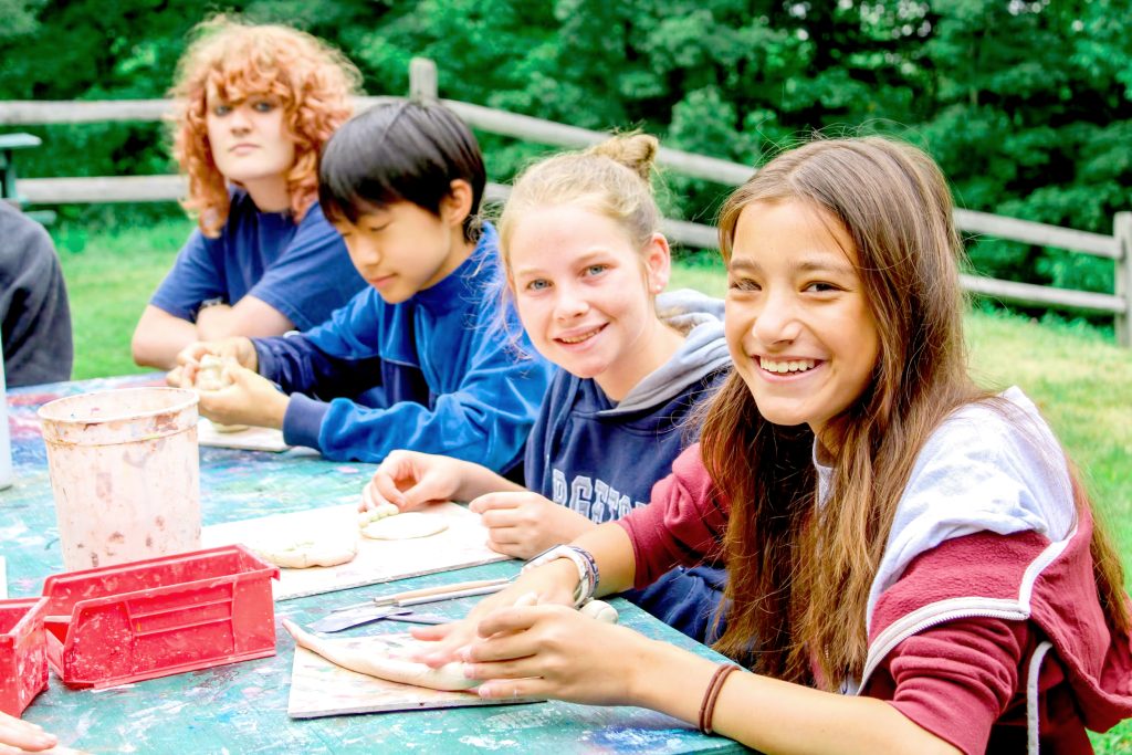 A camper works on an arts and crafts project at a table with a counselor