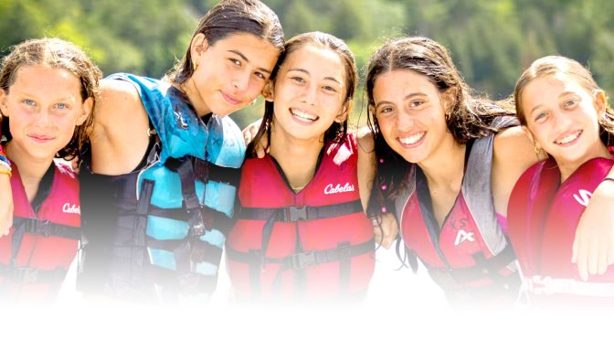 Four campers in life jackets smiling together by the water