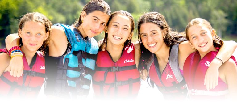 Four campers in life jackets smiling together by the water