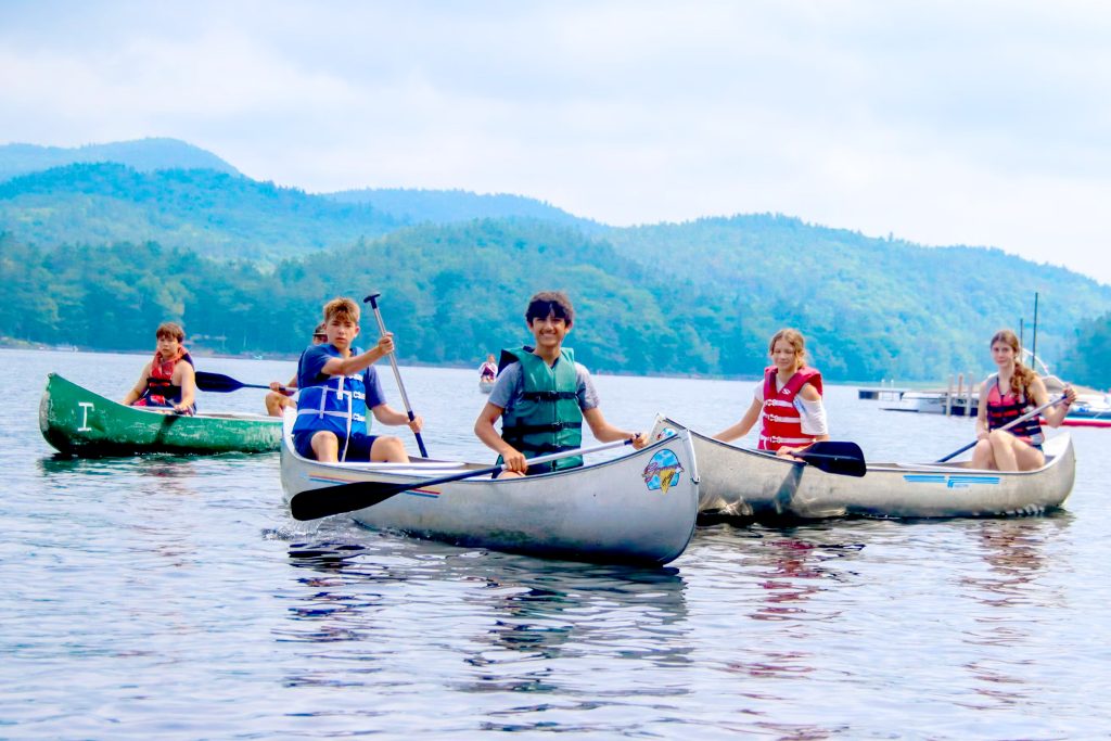 A canoe group paddles together on a calm lake at summer camp