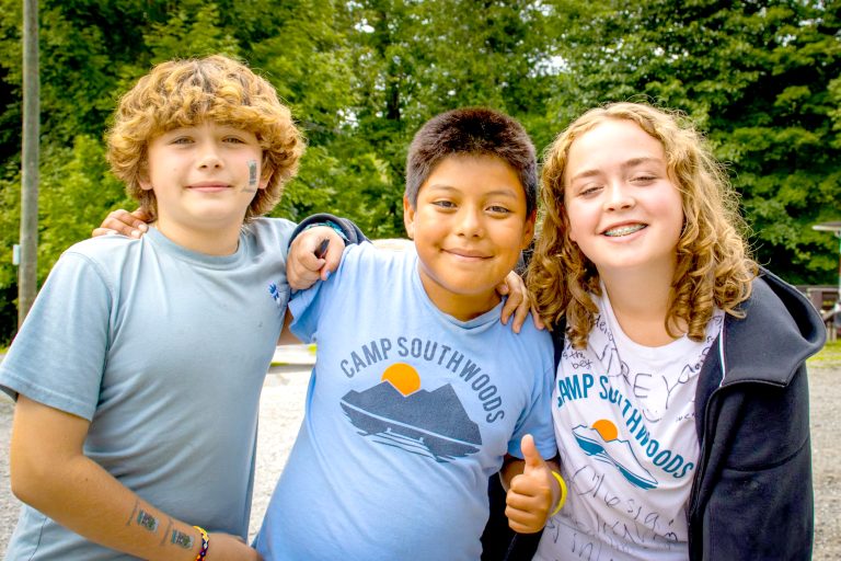 Three smiling campers standing together at overnight camp