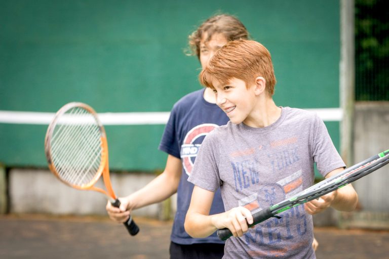 A camper serves during a tennis drill on an outdoor court