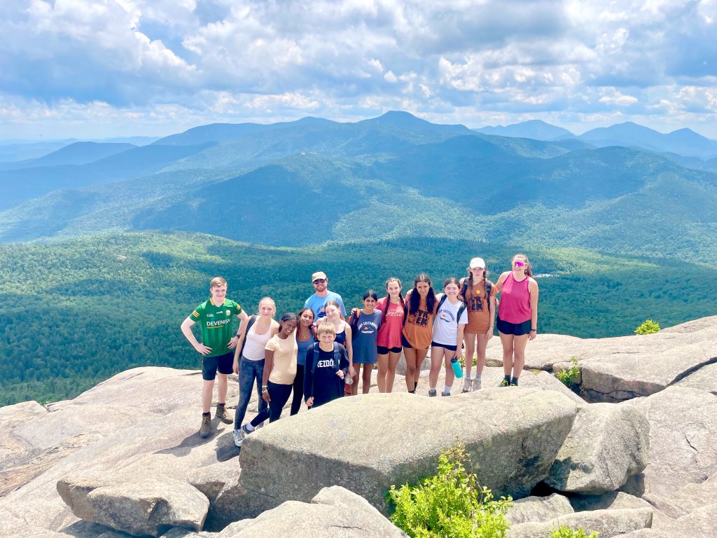 A group of campers pose together after reaching a mountain summit on a camp hiking trip