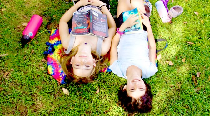 Two campers relaxing and laughing together in the grass at camp