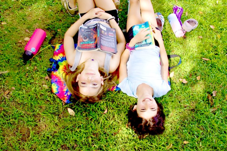 Two campers relaxing and laughing together in the grass at camp