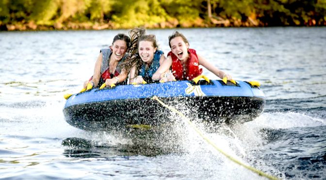 Three girls laughing together while tubing on the lake at camp