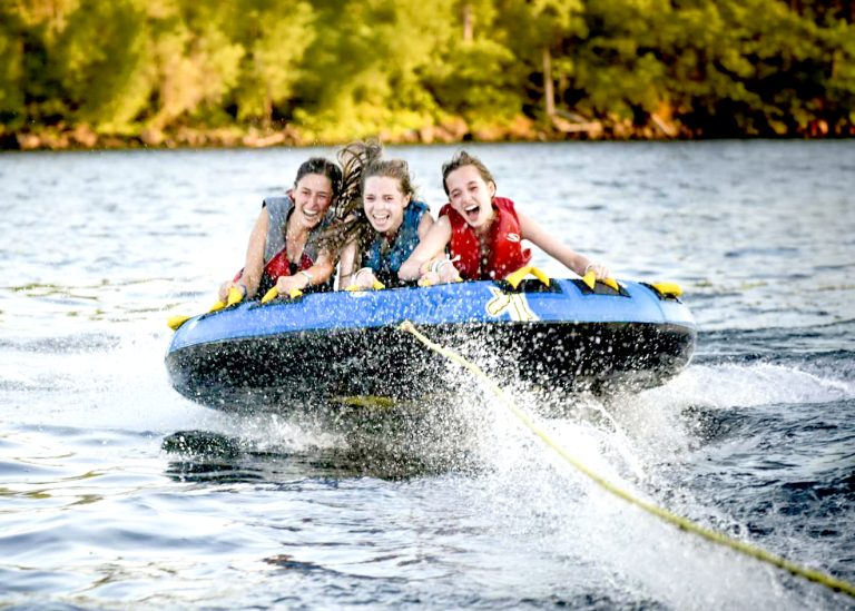 Three girls laughing together while tubing on the lake at camp