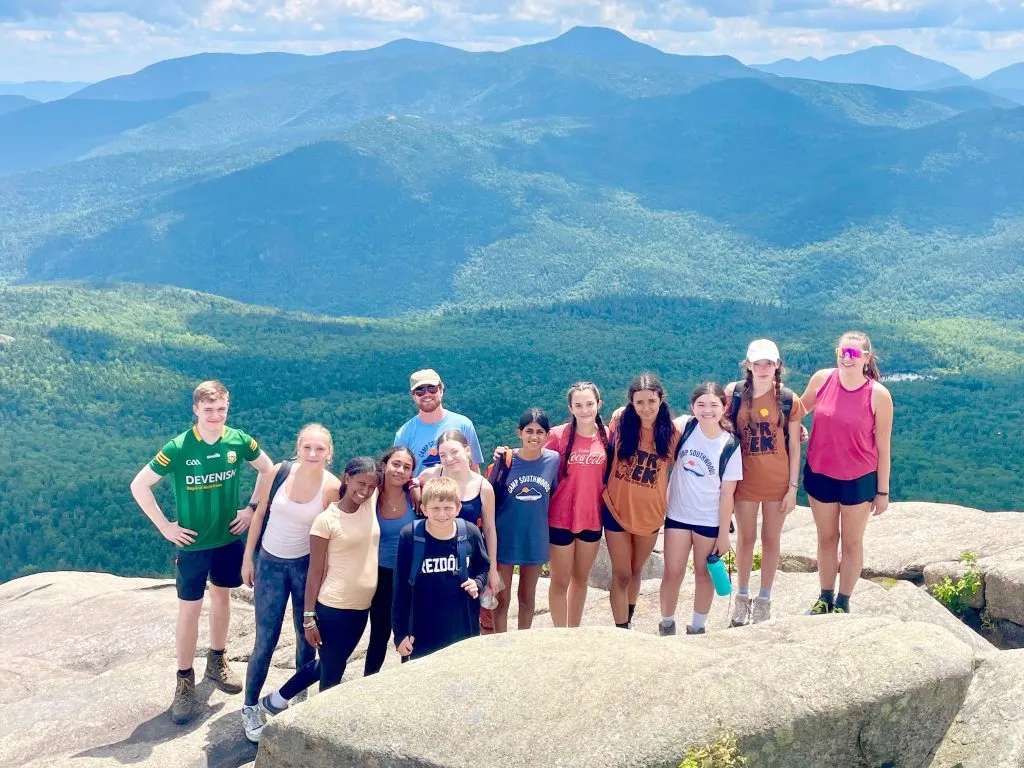 A group of campers pose together after reaching a mountain summit on a camp hiking trip